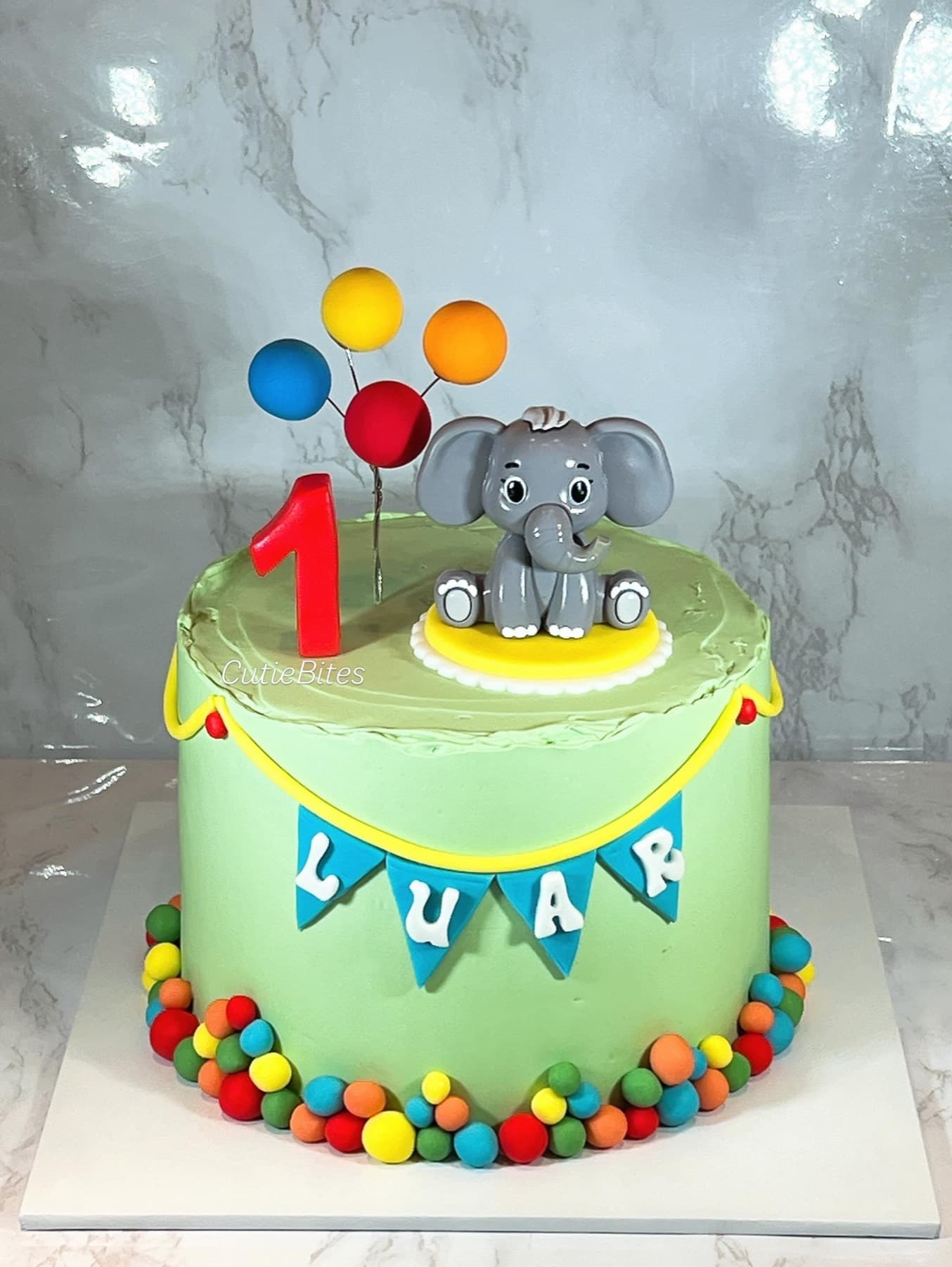 Green elephant first birthday cake with balloons, bunting and candy border — Cutie Bites, Orpington