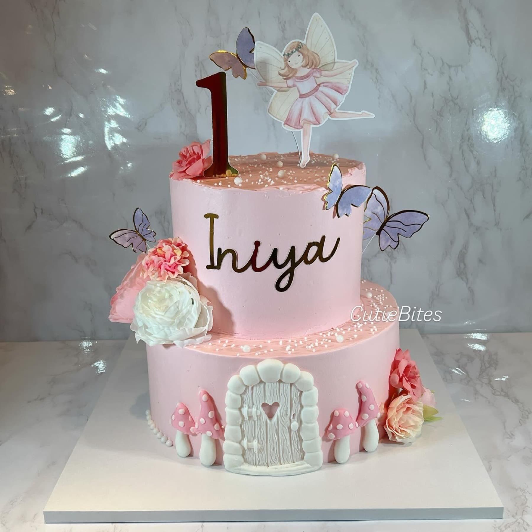 Two-tier fairy garden birthday cake with toadstools, fairy door and butterflies — Cutie Bites, Orpington