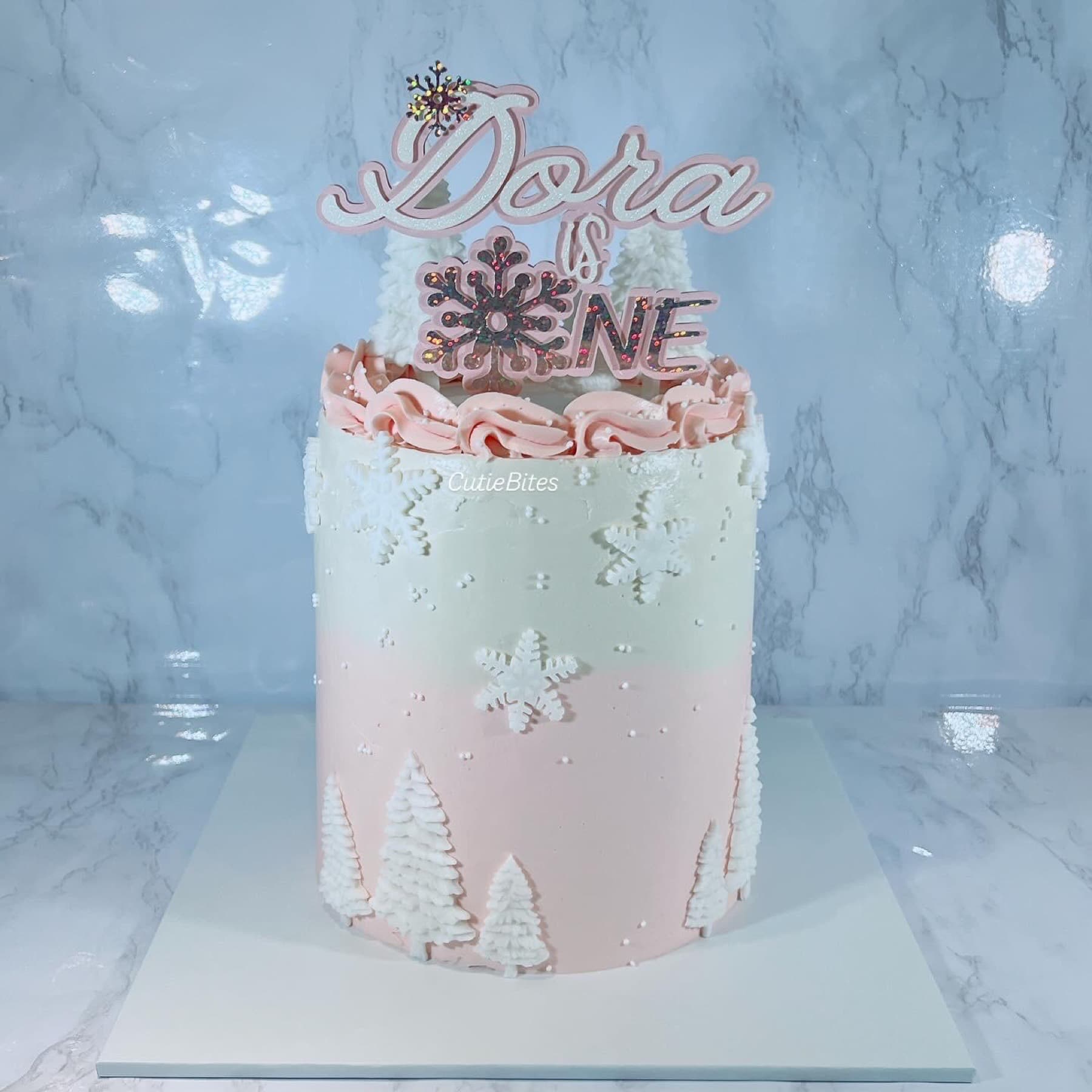 Pink winter wonderland birthday cake with snowflakes and white trees — Cutie Bites, Orpington