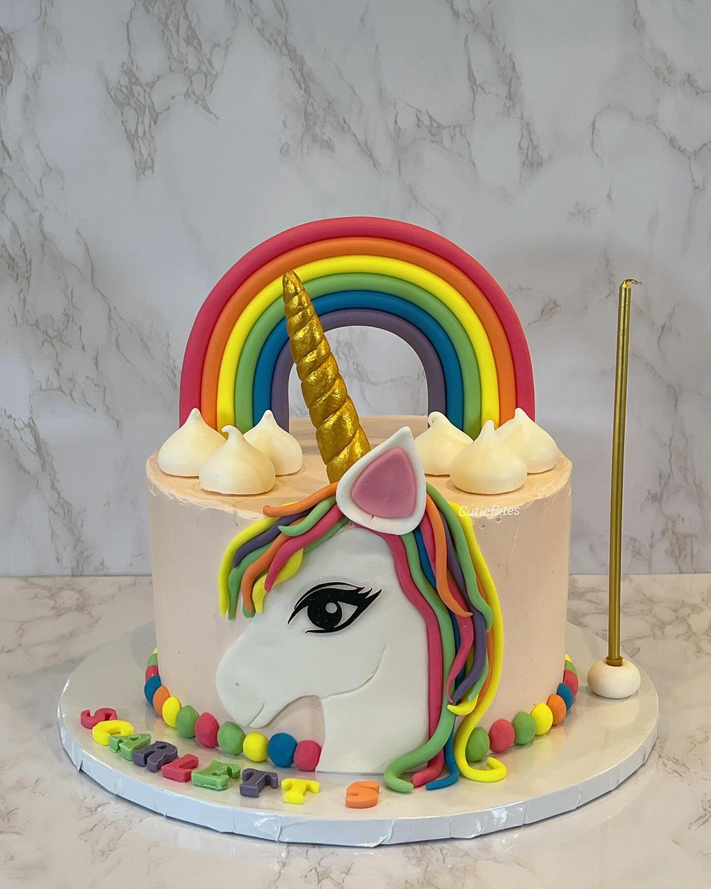 Unicorn cake with rainbow and gold horn on a marble background